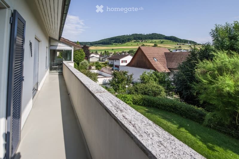 white concrete balcony, beige tiles, stone railing, outdoor access, views of a garden and houses in the background