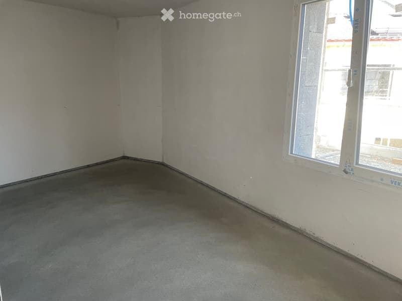 Empty room with bare concrete walls and floor, featuring a large window on one side.