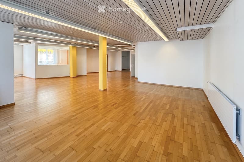 Unfurnished Room. Empty room with wooden flooring, white walls, and a central column. The space is well-lit with natural light from a window and recessed ceiling lighting.