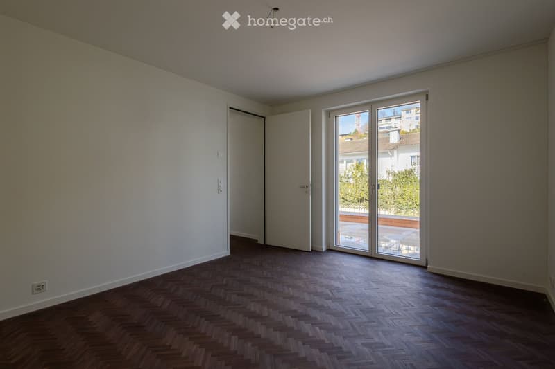 Modern room with white walls, wooden floor, white door, sliding glass door to terrace