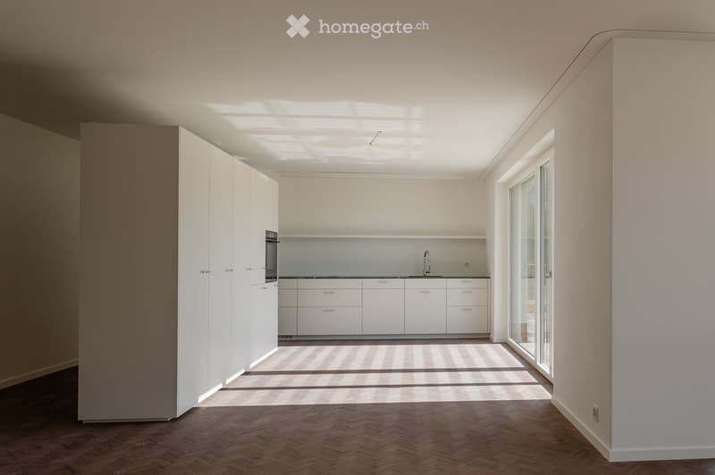 Minimalist kitchen with white cabinets, modern countertops, stainless steel faucet, and sliding glass doors leading to a patio