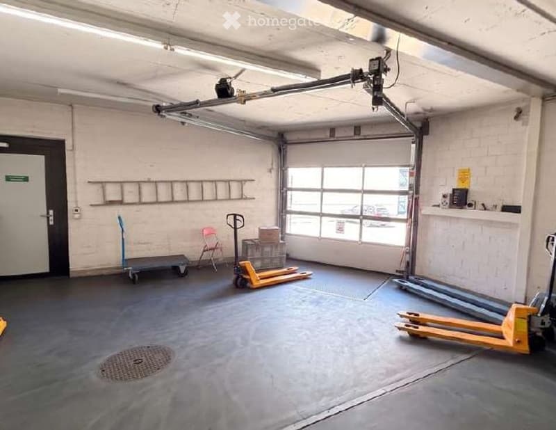 Other. {"visible_features": ["Garage"], "type": "Garage", "objects": [], "description": "Empty garage with white brick walls, large overhead door, and industrial shelving. Contains a few storage items like a ladder, hand truck, and pallet jack.", "localiz