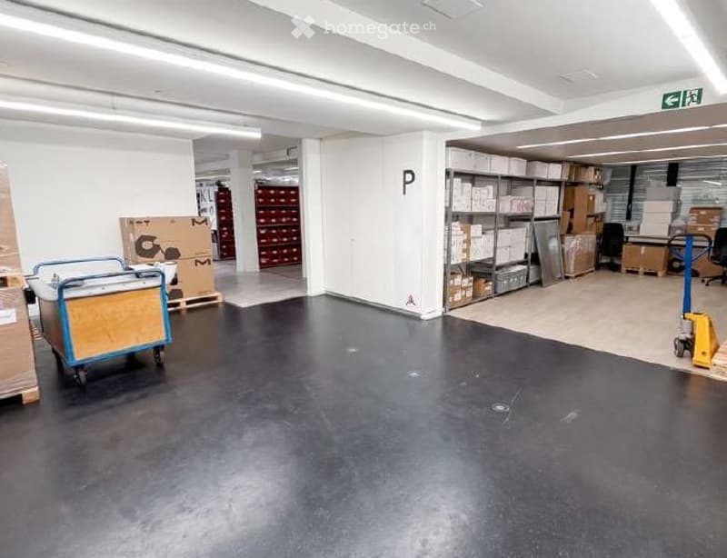 Unfurnished Room. Empty warehouse or storage space with a smooth black floor, white walls, and industrial shelving units filled with boxes and supplies. The area is well-lit with fluorescent lighting, and there are some storage carts and a yellow dolly vi