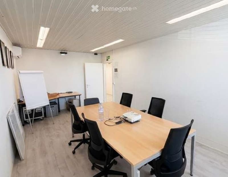 Furnished Room. A modern, well-lit meeting room with a large wooden table surrounded by black office chairs, a whiteboard, and a projector on the table.