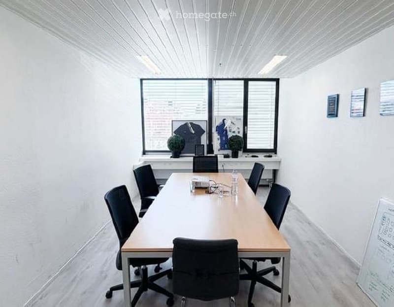 Furnished Room. Bright, modern conference room with a long wooden table, black chairs, a large window with blinds, and a small plant on the windowsill.