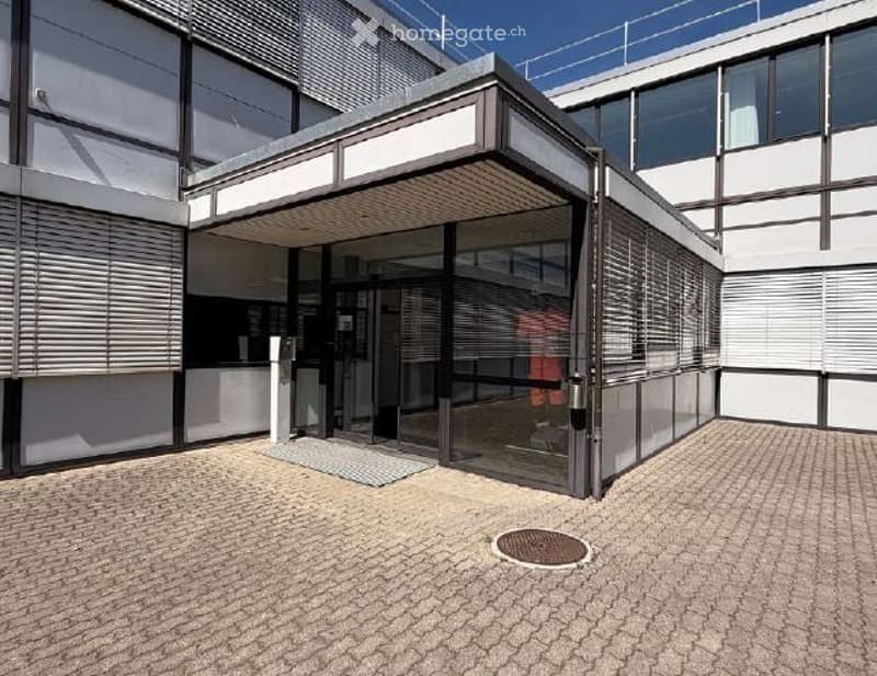 Building. Modern building entrance with glass doors, brick pavement, and a covered walkway.