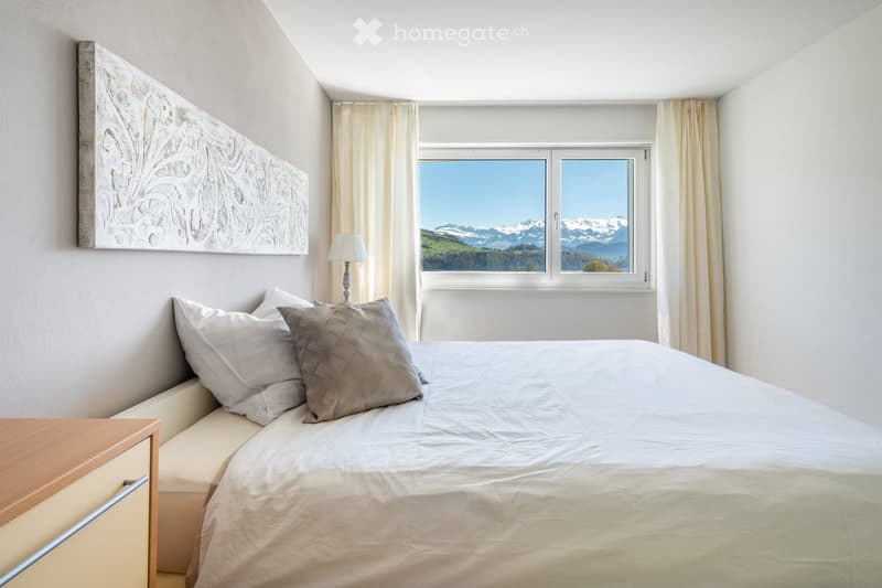 Bedroom. Modern bedroom with a large bed, pillows, nightstand, lamp, and scenic mountain view through large windows.