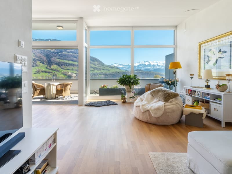 Furnished Room. Bright living room with large windows offering a scenic mountain view, featuring a white sofa, a round table with chairs, a floor lamp, a television, and a bookshelf.