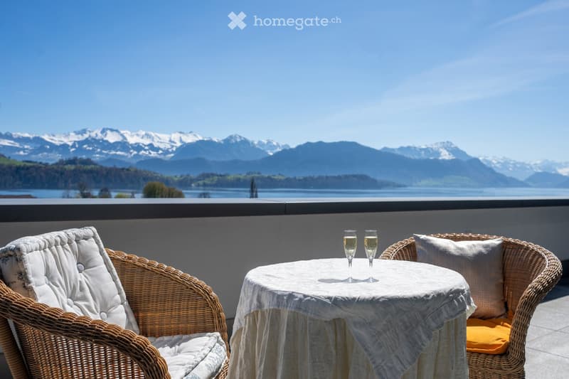 Balcony / Terrace. Balcony with a scenic mountain and lake view, featuring a small round table with two wine glasses and two wicker chairs.
