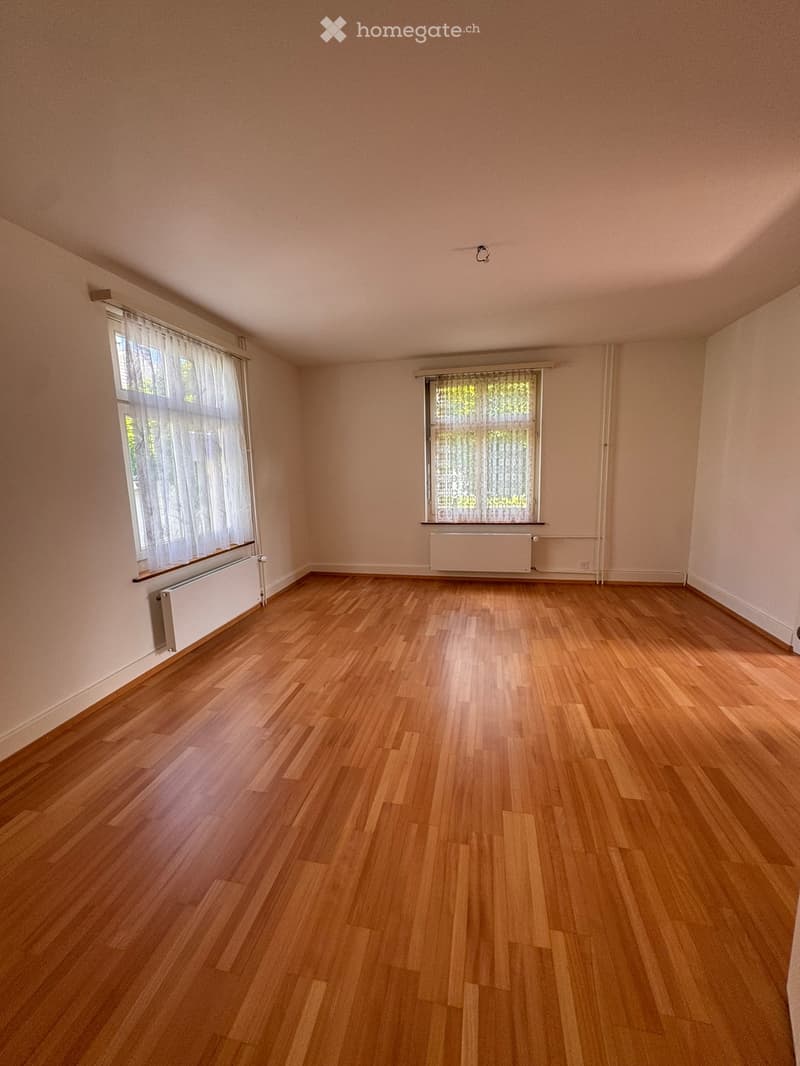 Unfurnished Room. Empty room with wooden flooring, light-colored walls, and two windows with white curtains. Radiators are visible beneath each window.