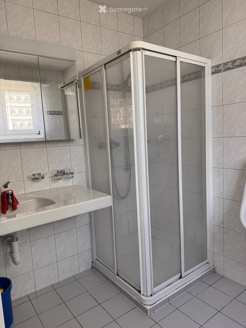 Bathroom. Modern bathroom with white tiles, a glass-enclosed shower, a white sink with a mirror, and a red towel hanging on the faucet.