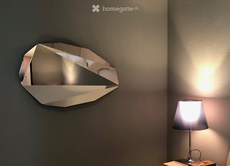 Furnished Room. A modern interior corner with a geometric wall-mounted mirror and a table lamp on a small table.