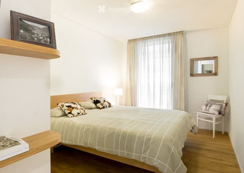 Bedroom. Cozy bedroom with a double bed, patterned pillows, a wooden chair, a mirror, and a shelf with a picture frame and book.