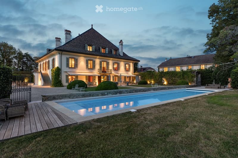 House. Spacious villa with large swimming pool, trees, and open lawn in the front, illuminated at night