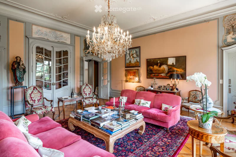 Living Room. Elegant living room with pink sofa, coffee table, ornate chairs, chandelier, and artwork.