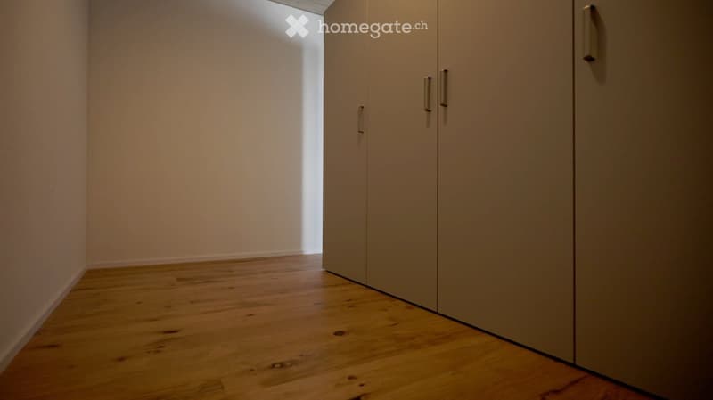 Unfurnished Room. Empty hallway with wooden flooring and light-colored walls, featuring a set of closed double doors on the right side.