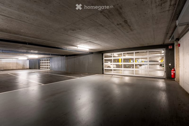 Building. Underground parking area with concrete walls and ceiling, marked parking spaces, and a large garage door leading to another level.
