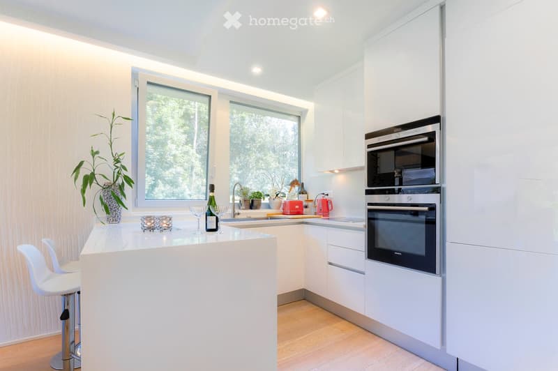 Kitchen. Modern kitchen with white cabinets, stainless steel appliances, island with bar stools, and decorative items on the counter.