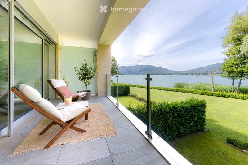 Balcony / Terrace. Balcony with sun loungers, cushions, a small table, and a potted plant, overlooking a scenic lake and mountains.