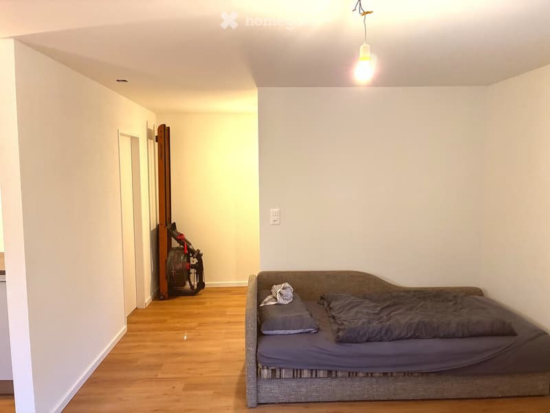 Empty room with wooden floor, white walls, a bed, and a light fixture