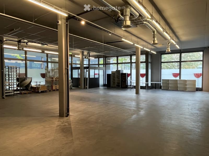 Unfurnished Room. Large, open, industrial-style space with concrete floors, exposed metal beams, and large windows allowing natural light. Minimal furnishings include a few storage units and a small table near the windows.