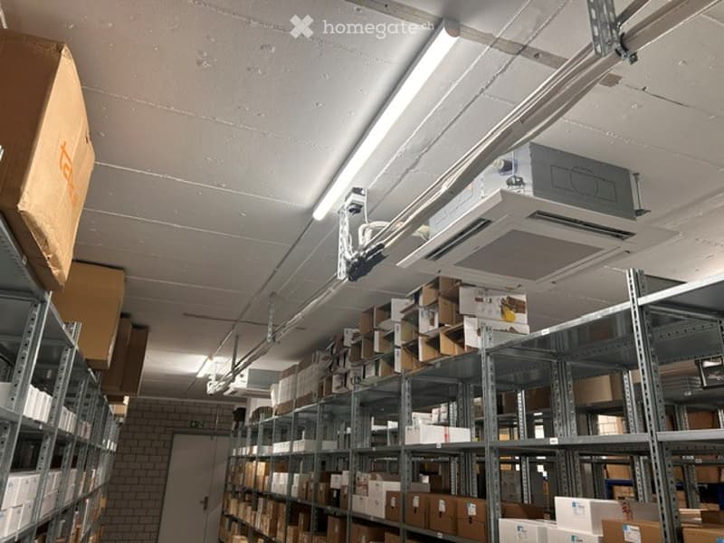 Other. Warehouse space with metal shelving units filled with cardboard boxes, fluorescent lighting, and an air conditioning unit mounted on the ceiling.