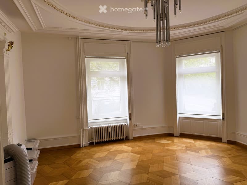 Unfurnished Room. Empty room with wooden parquet flooring, large windows, radiator, and ornate ceiling with a chandelier fixture.