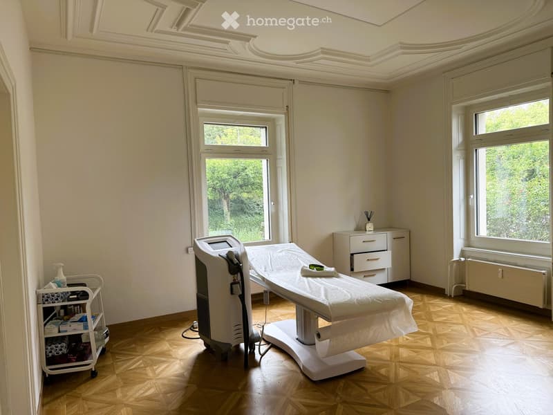 Furnished Room. Bright, well-lit room with wooden flooring, large windows, a treatment table, a cart with supplies, and a cabinet.