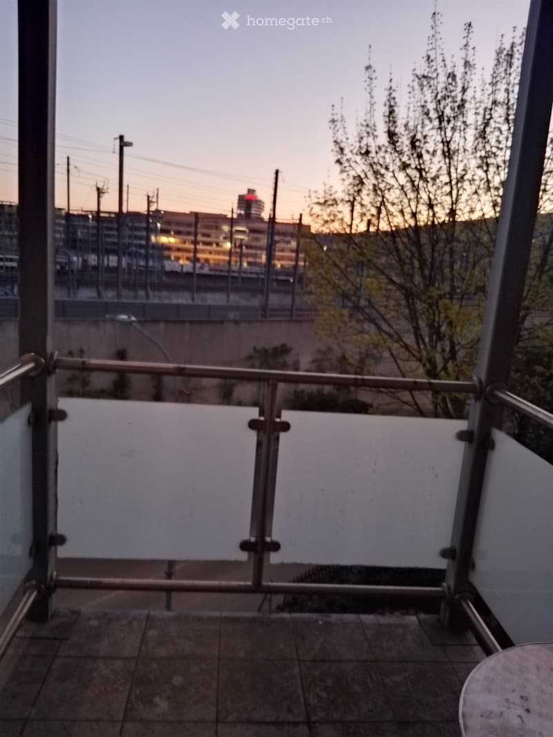 Balcony with metal railings, glass wall, tiled floor, view of a city skyline