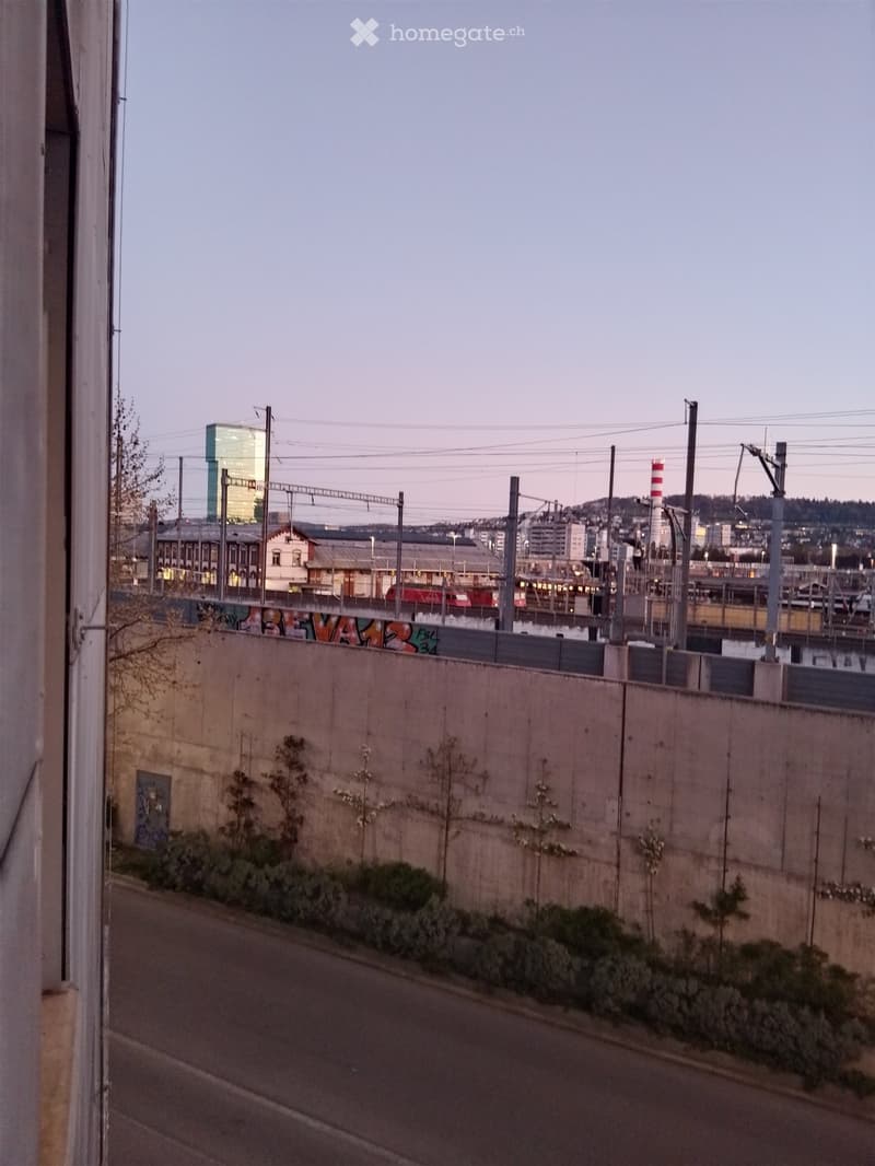 View of a city with a train station, buildings, and a road with a concrete barrier
