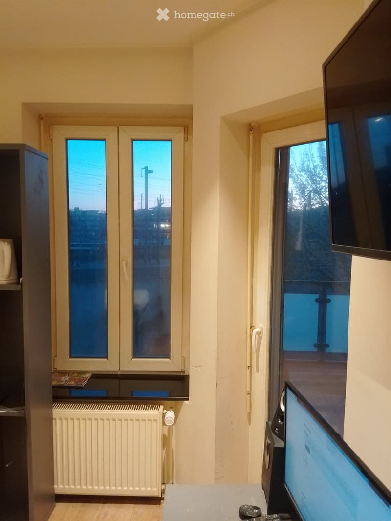 room with two windows, wooden floor, white radiator, desk with computer, speakers, cabinet