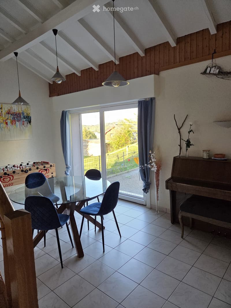 Furnished Room. Dining area with a glass table, blue chairs, a piano, and a small football table. Large windows with curtains lead to a view of the garden.