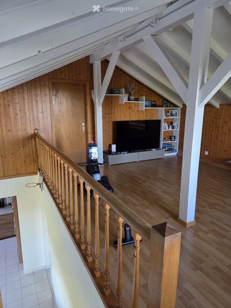 Furnished Room. Open living space with wooden floors, wooden staircase, television, shelves, and exercise bike.
