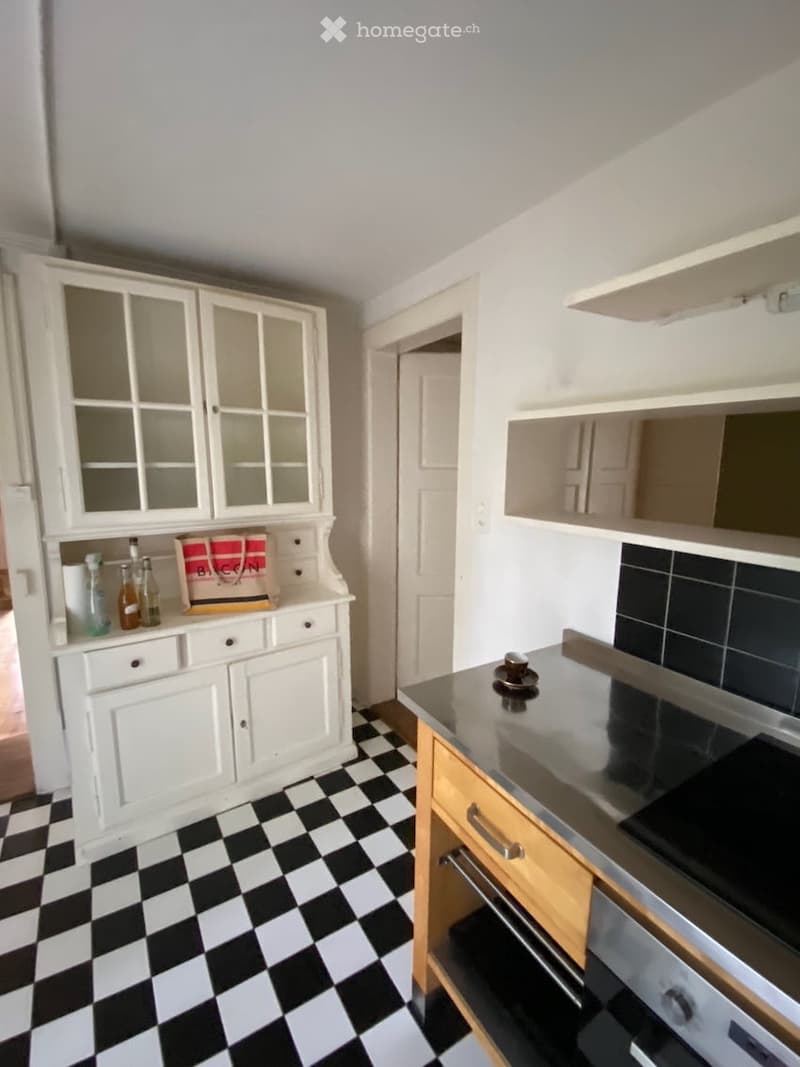 Kitchen. A small kitchen with white cabinets, a black and white checkered floor, and a stainless steel oven. A handbag and a cup are placed on the counter.