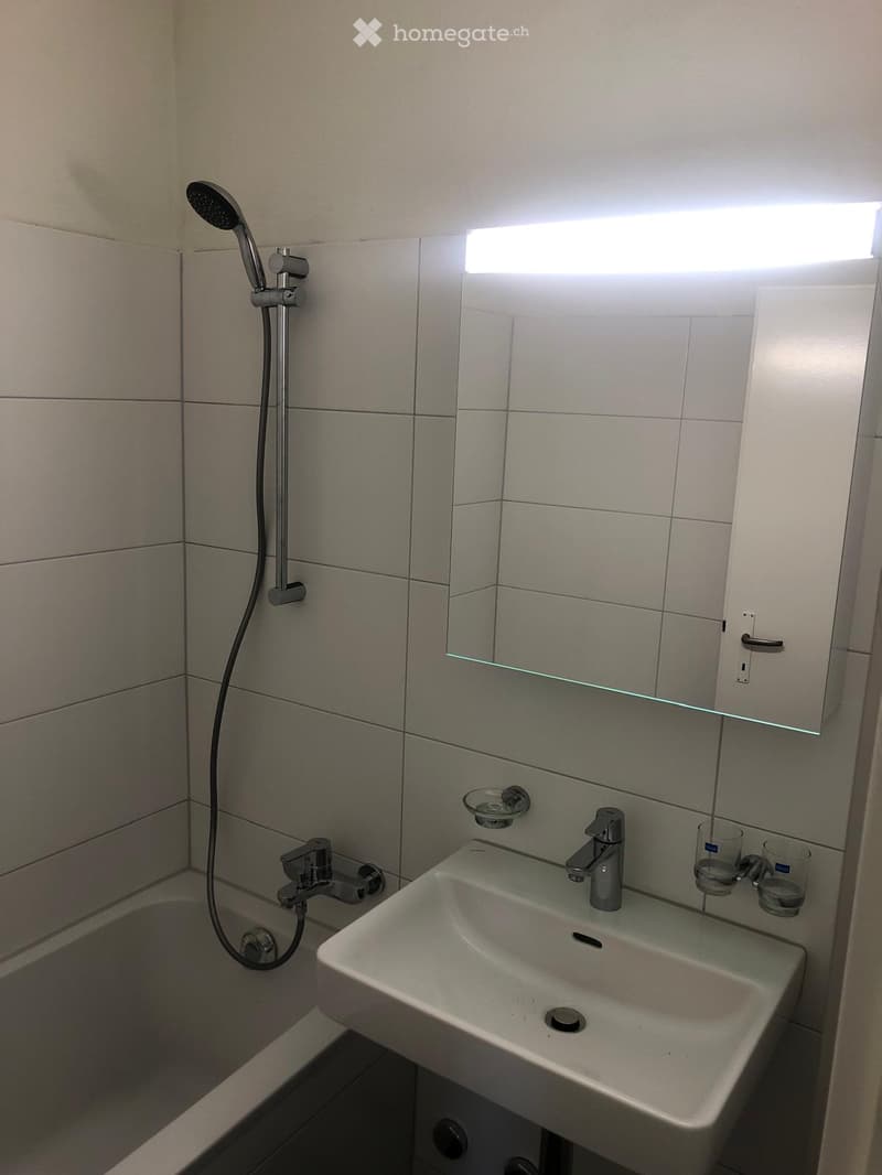 Bathroom. Modern bathroom with a bathtub, sink, mirror, and showerhead. The sink has two cups placed on the counter.