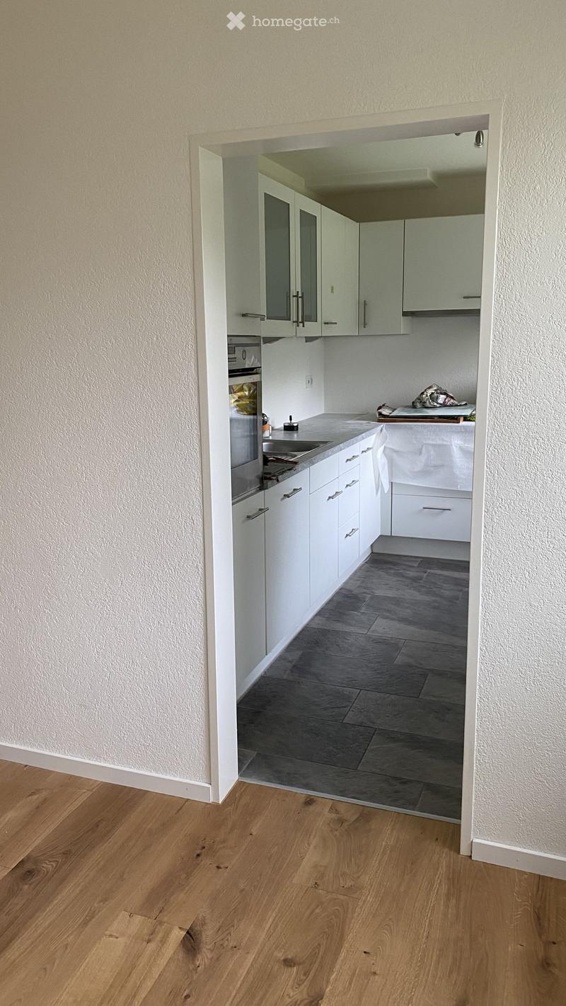 Kitchen. Modern kitchen with white cabinets, stainless steel sink, and grey tiled floor. Wooden flooring visible in the adjacent area.