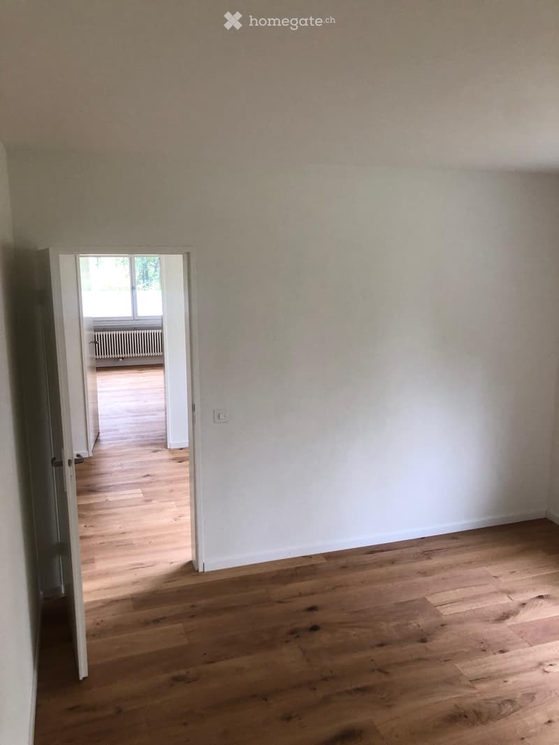 Unfurnished Room. Empty room with light wooden flooring and white walls, featuring an open doorway leading to another room with a radiator and window.