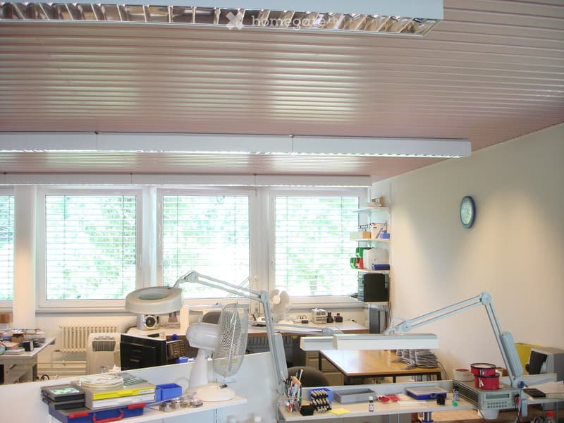 Furnished Room. Well-lit room with multiple tables, fans, lamps, shelves, and various office supplies.