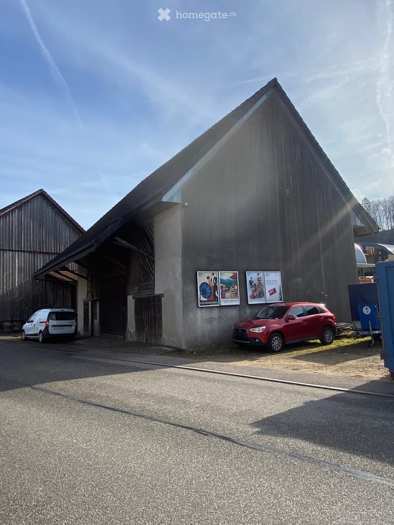 Building. Large industrial-style building with a triangular roof, posters on the wall, and two parked cars in front.
