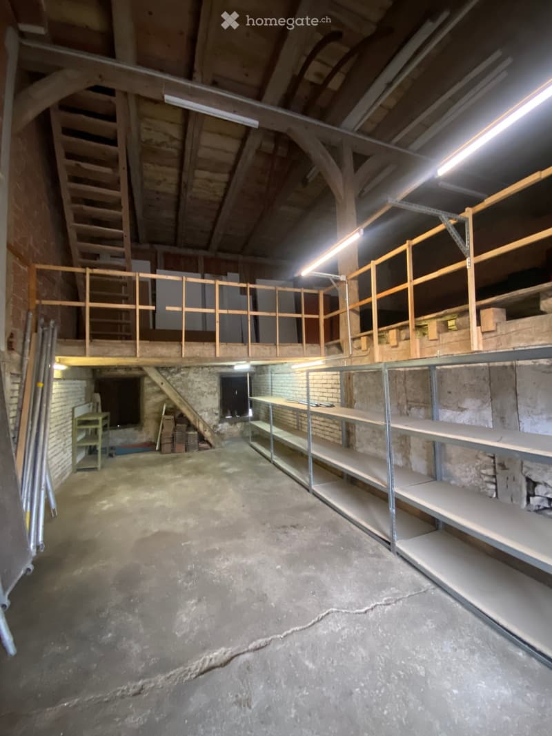 Unfurnished Room. Empty attic space with exposed wooden beams, concrete floor, metal shelving units, and a small green table near the entrance.