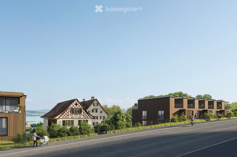 Building. A modern residential complex with a mix of contemporary and traditional-style buildings, surrounded by greenery and a clear view of a lake in the background.