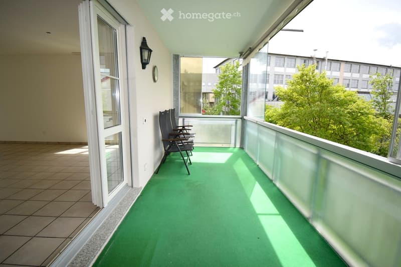Balcony / Terrace. Balcony with green carpeting, two black chairs, large windows, and a view of trees and buildings.