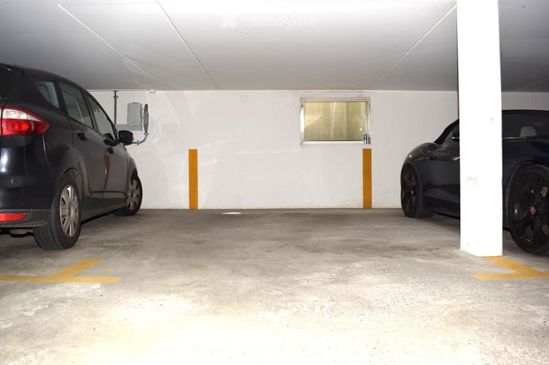 Building. Underground parking area with two parked cars, concrete floor, white walls, and yellow parking lines.