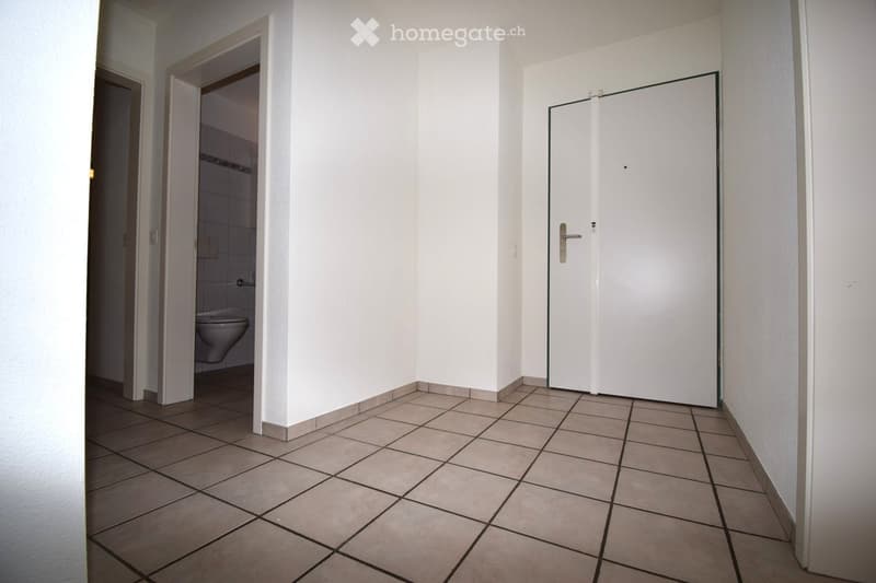 Corridor / Hallway. Empty hallway with tiled floor, white walls, and two doors, one leading to a bathroom with a toilet visible.