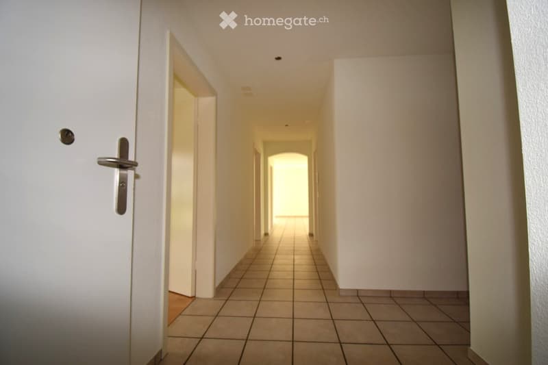 Corridor / Hallway. Empty hallway with tiled floor, white walls, and a closed door on the left side.
