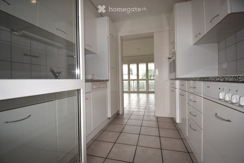 Kitchen. Modern kitchen with white cabinets, stainless steel appliances, tiled floor, and a view to a balcony area through large glass doors.