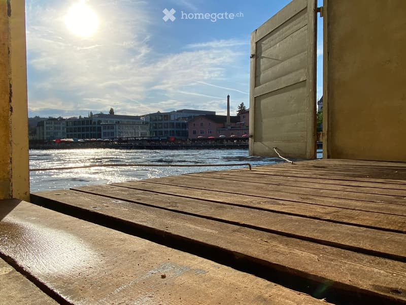 Balcony / Terrace. Wooden balcony overlooking a waterfront with buildings and a clear blue sky in the background.