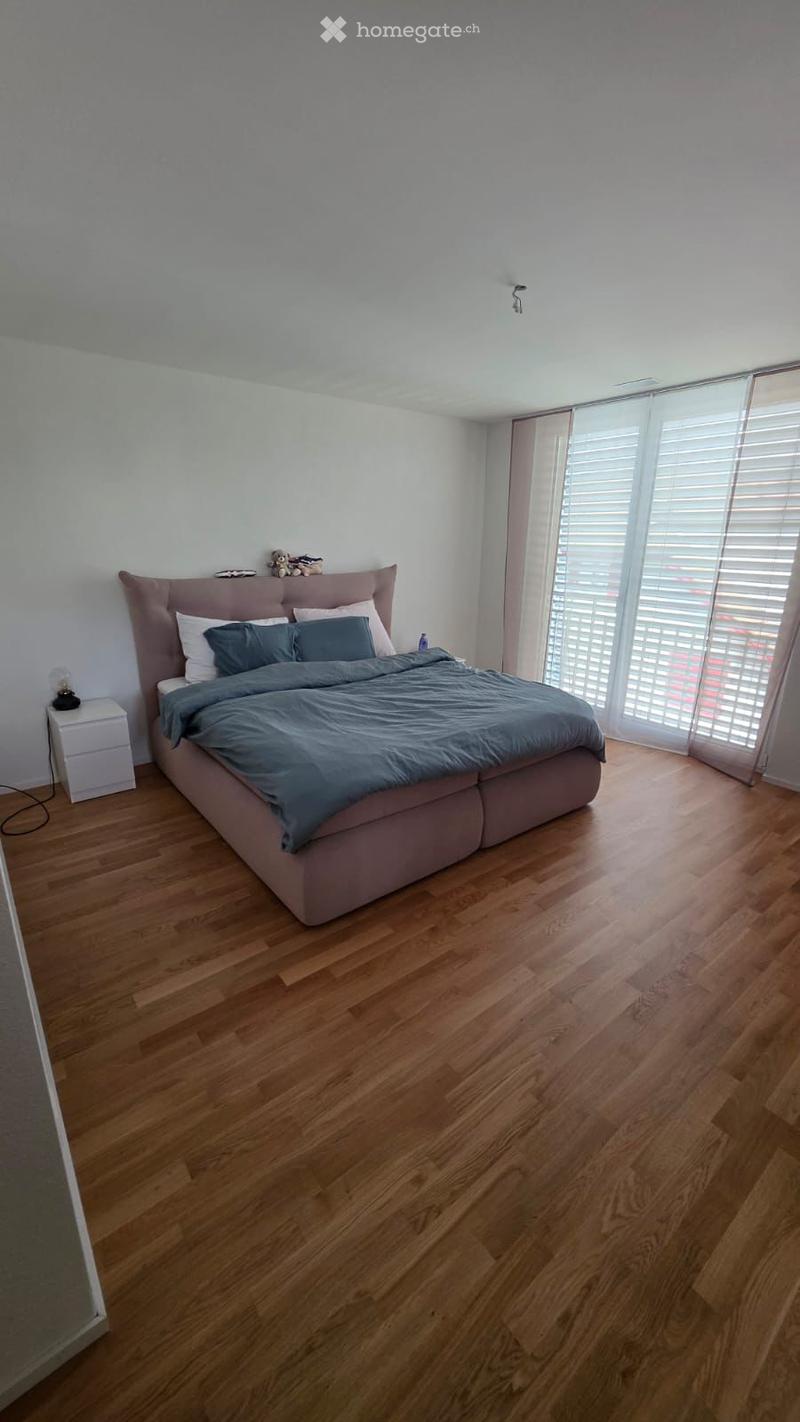 Bedroom. Modern bedroom with wooden flooring, large bed with grey bedding, nightstand with lamp, and decorative items on the headboard.