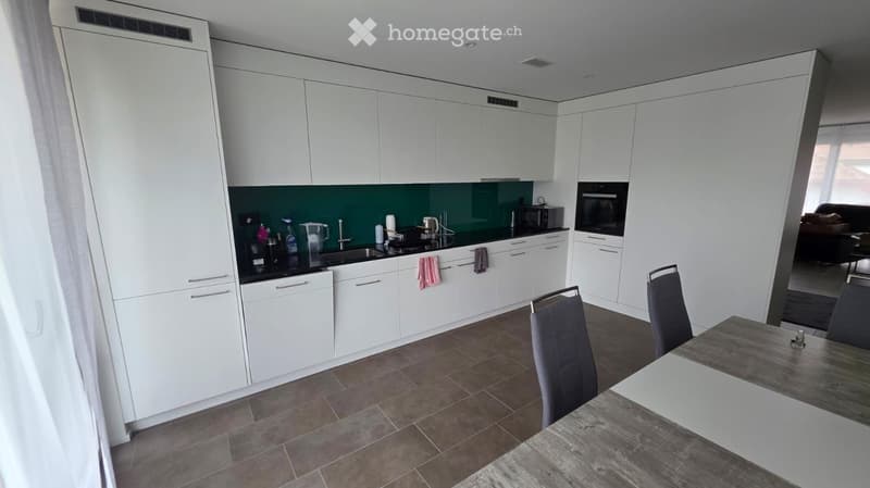Furnished Room. Modern kitchen with white cabinets, stainless steel appliances, and a dining area with a table and chairs.