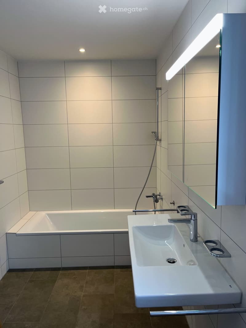 Modern bathroom with white tiles, bathtub, shower, and sink.